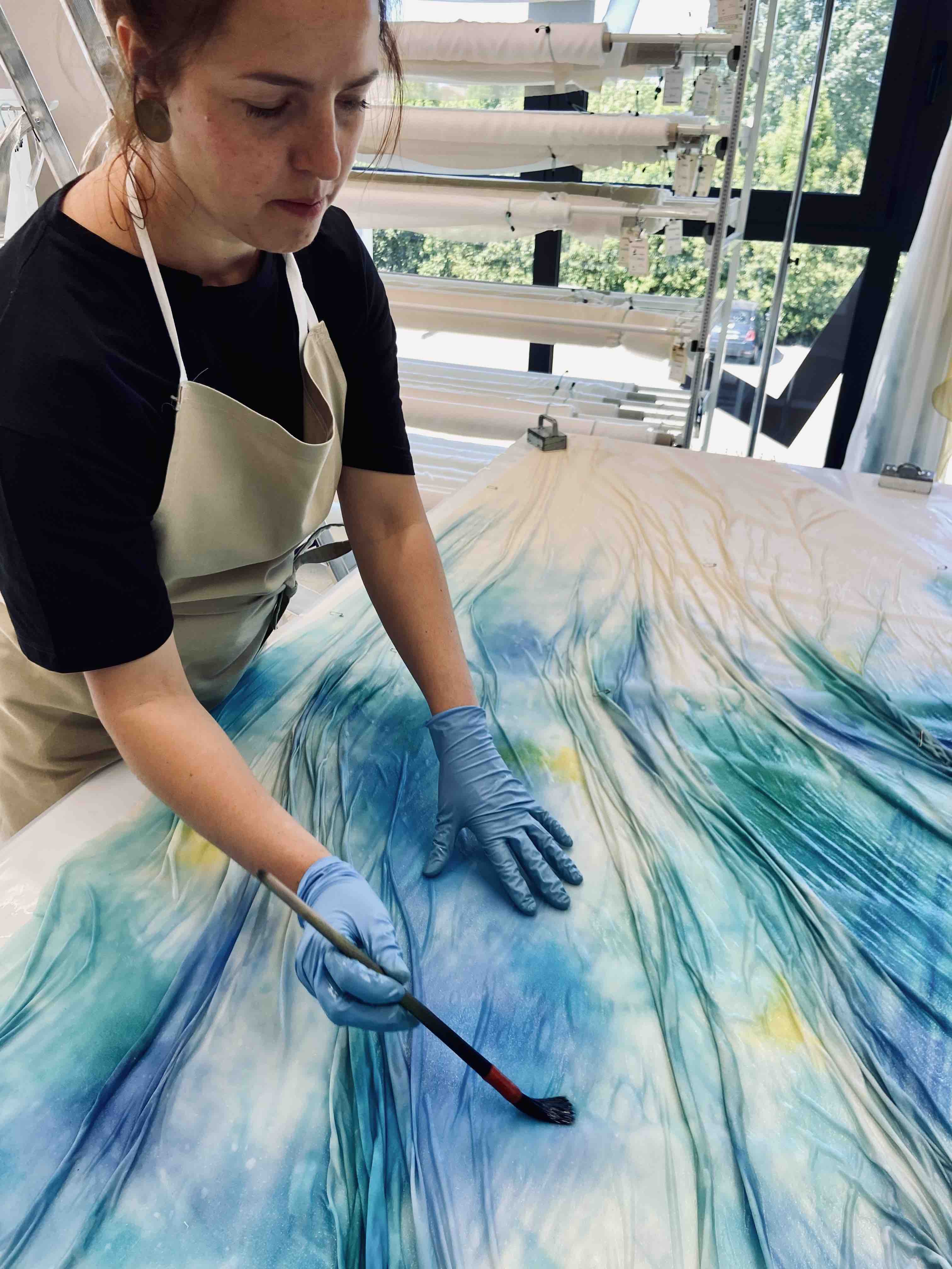 Larimeloom designer Maria Lucia Squillari hand-painting the bottom of a wedding dress skirt in blue and yellow hues, showcasing her expertise in color wedding dresses